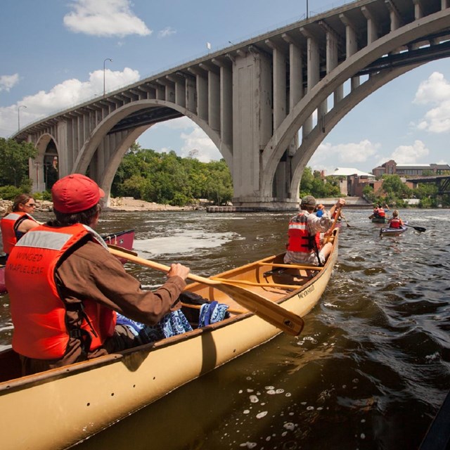 Group of canoers on a river under an arched bridge