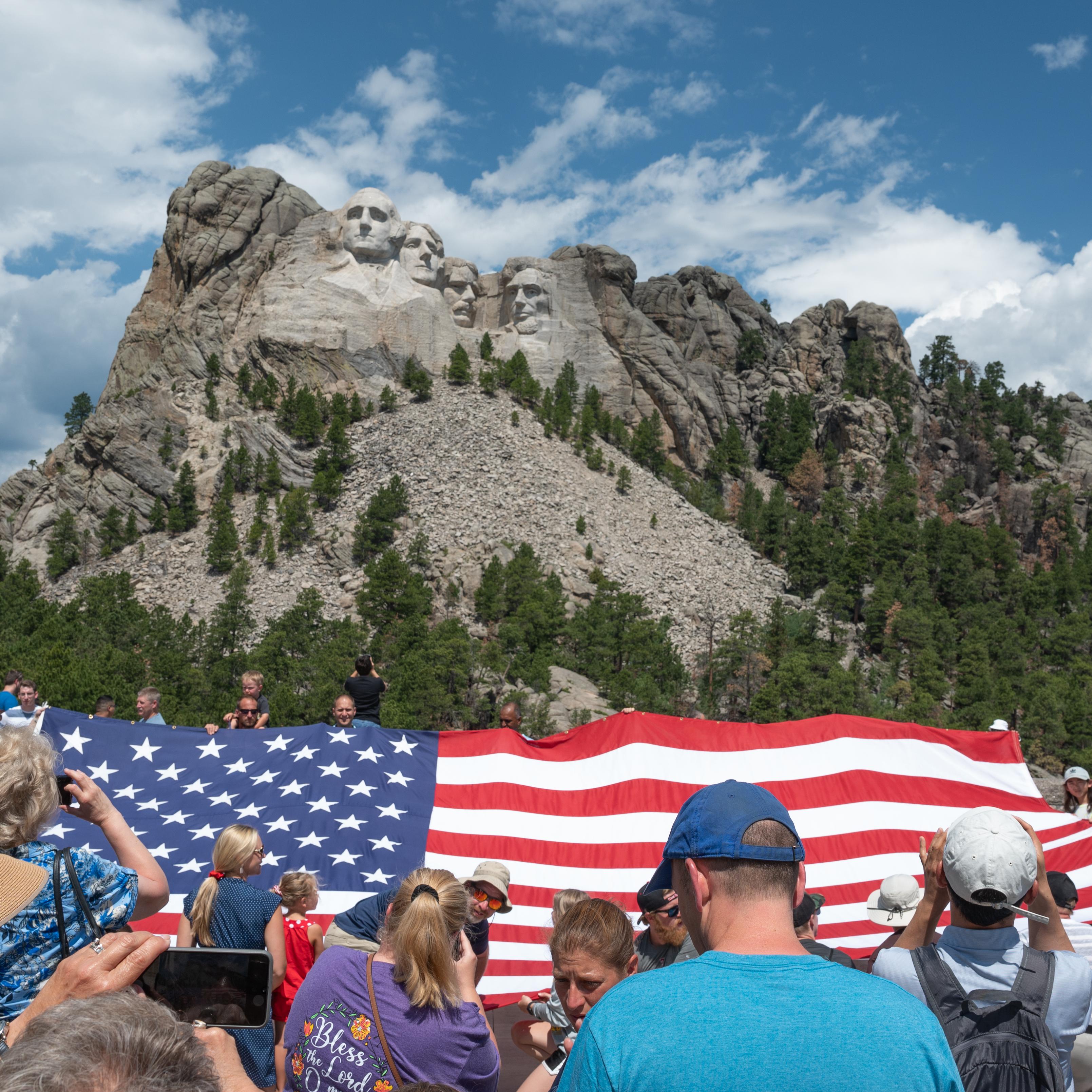 Group of people holding up an enormous American flag in front of Mount Rushmore