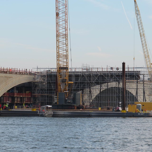 Large construction equipment near and on a stone bridge