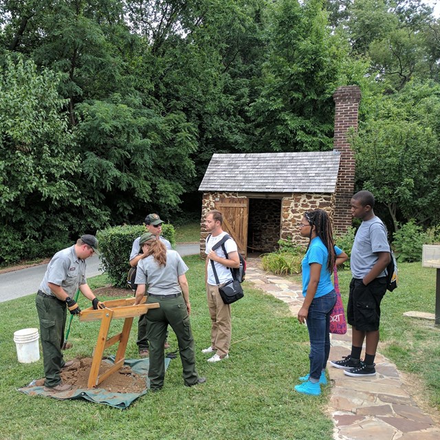 Acheologists around a screen outside a historic house talking to visitors 