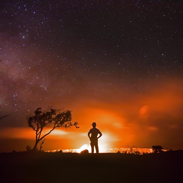 Silhouette of person against a lava eruption at night