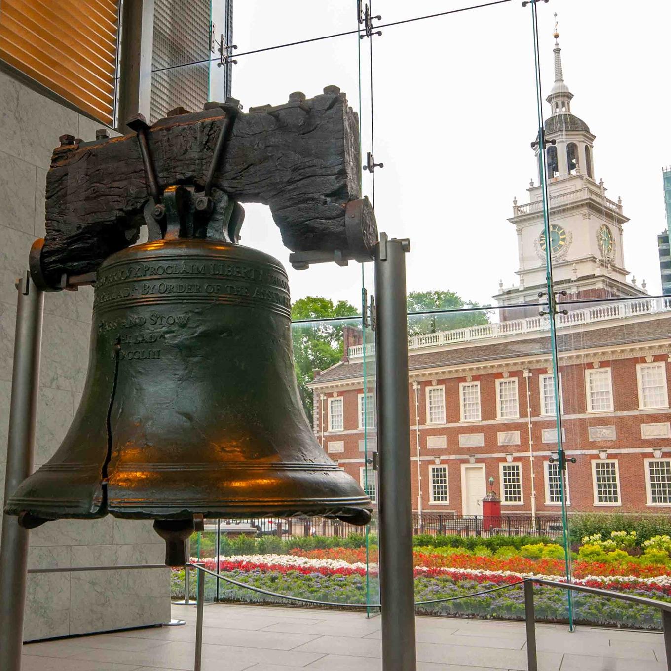 Liberty Bell in front of a window to Independence Hall outside