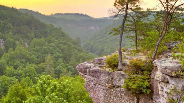 A rocky cliff reaching out from the corner with a sunset in the background.