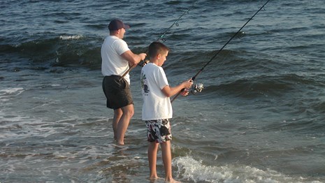father and son standing on the beach fishing in the ocean