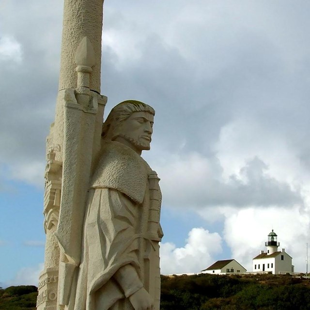 stone statue of Juan Rodriguez Cabrillo with hillside and clouds in background