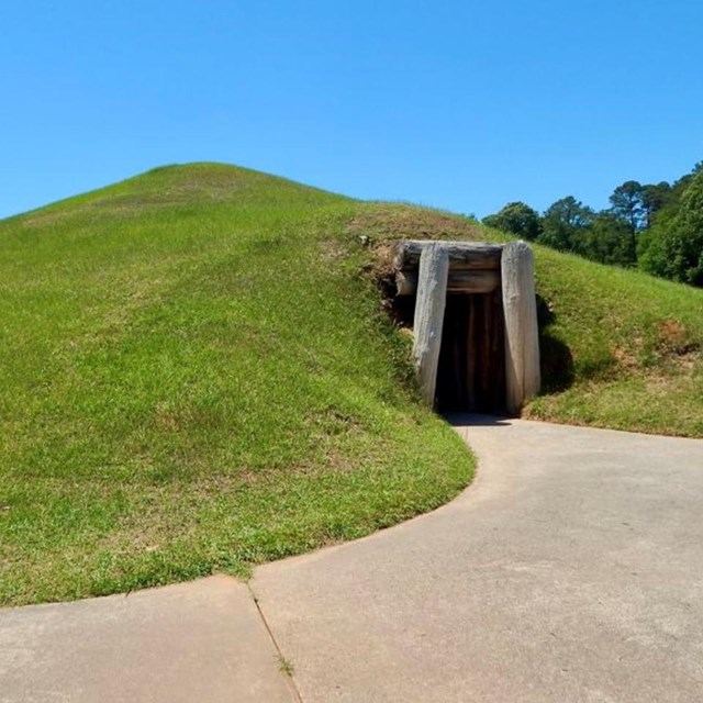 NPS Photo of the Earth Lodge entrance with a concrete pathway in front.