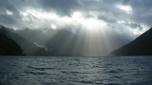 The sun breaks through clouds to shine down on a lake.