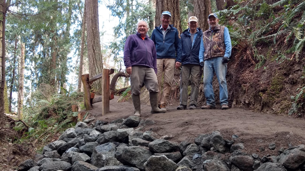 Volunteer trail crew standing proud in front of reinforcing rock wall built to hold up trail
