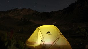 Lamp light glow within a yellow tent at night.