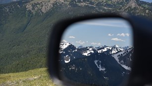 A view of the Olympic Mountains is reflected in a driver's side mirror.