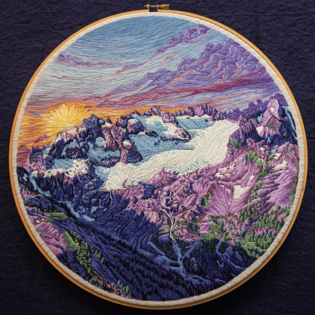 A detailed embroidered view of a golden sunset over a purple and white mountain glacier.