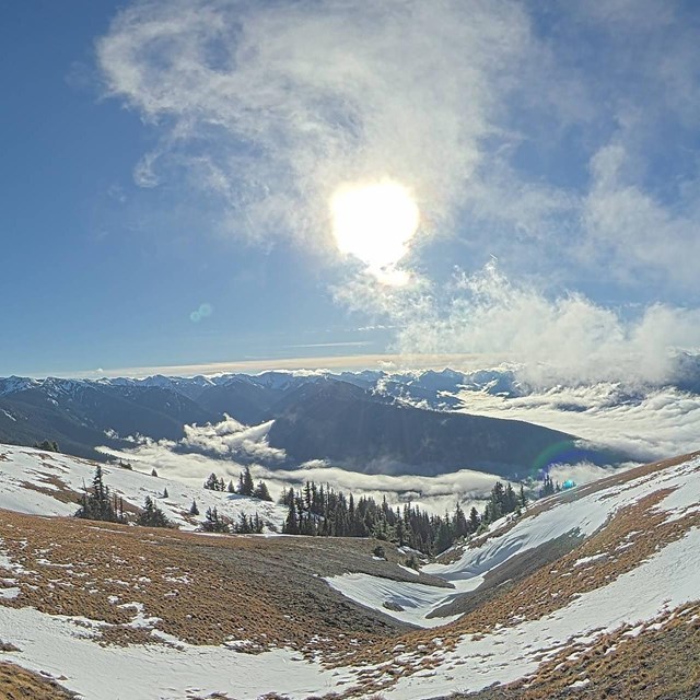 Mountain panorama under sunny skies, and a foreground hillside with patchy snow.