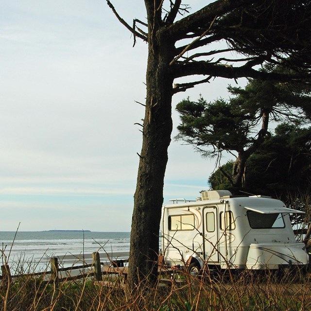 An RV sits on a windswept cliff near the ocean.