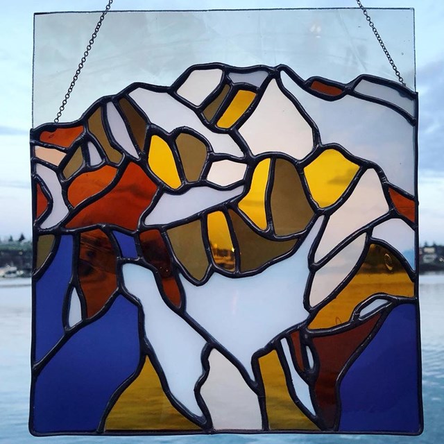 Two stained glass depictions of the same mountain peak. The glacier is much larger in the first.