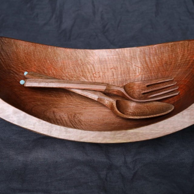 A hand carved wood bowl and serving utensils, wide and shining with a broad flat rim.