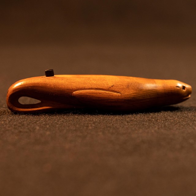 A small wooden tool carved in the shape of a seal, with two small parallel metal blades on its back.