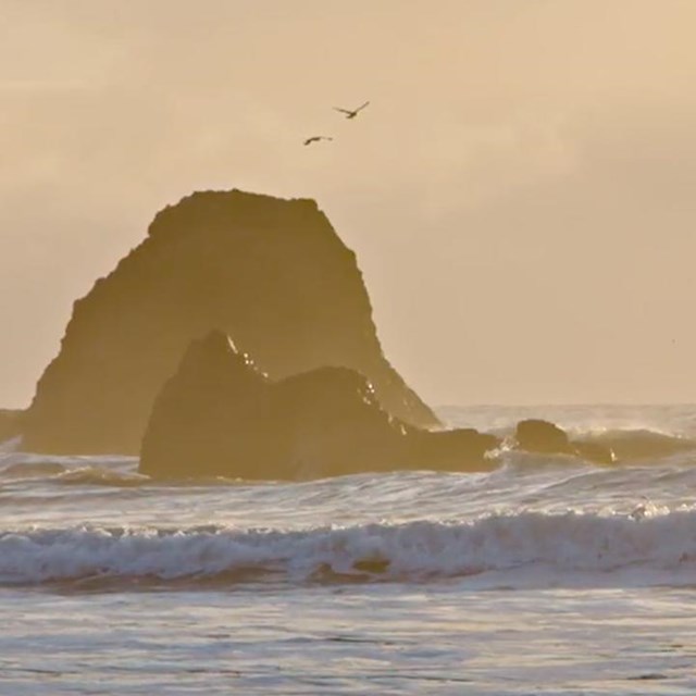 Waves crashing at sunset on a coast with sea stacks.