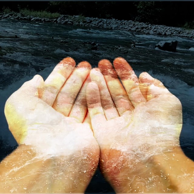 A pair of hands cupped together, superimposed over a flowing river.