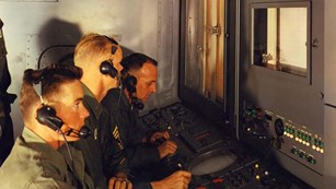 Uniformed operators with headsets seated in Nike Hercules battery control trailer, 1959.