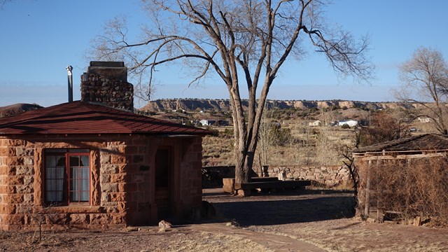 One-story brick structures, walkways, stone walls, and trees in the Hubbell Trading Post landscape.