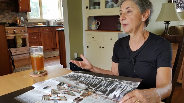 A women, seated at a dining room table, gestures over the park brochure in front of her.