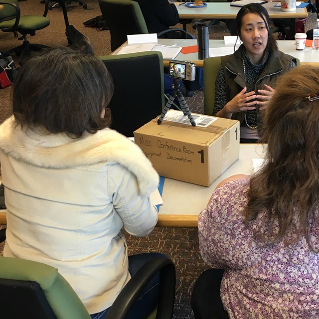 Three students at a table practice video recording interviews with each other during a workshop.