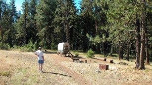 grassy area with dirt road, an emigrant wagon, and a woman