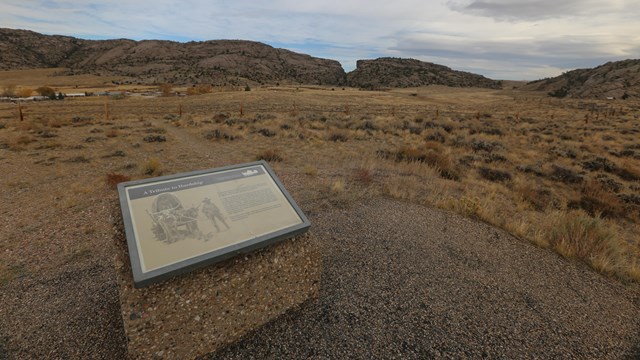 An interpretive exhibit sign sits facing out on an expansive desert view.