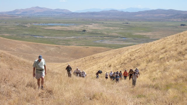 People walk up a ravine in grass-covered rolling hills.