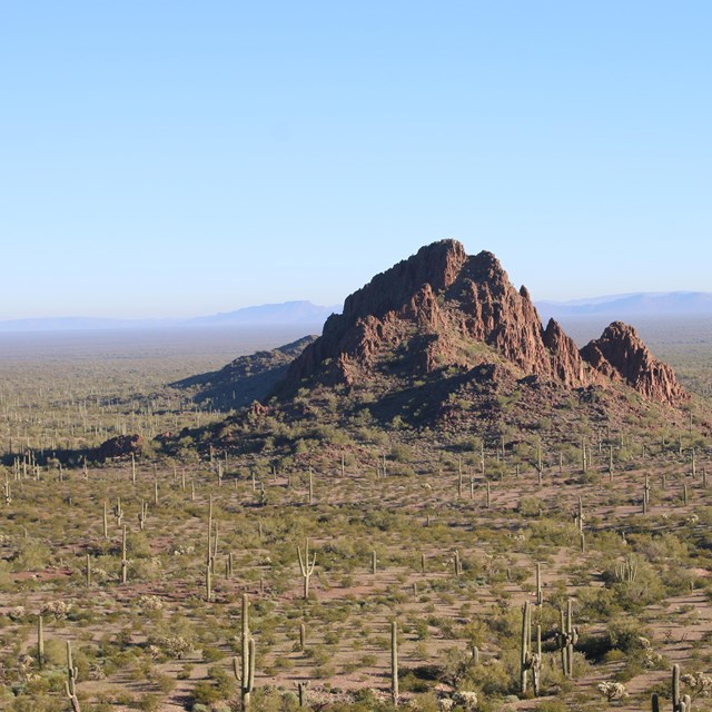 A mountain stands alone, rising up out of the ground, with long stretches of flat land on all sides.