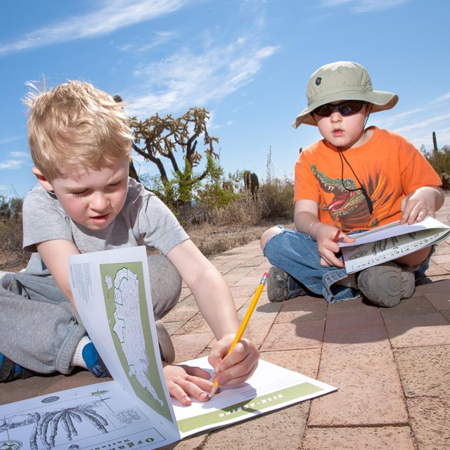 two children sitting on the brick path working on their junior ranger booklets