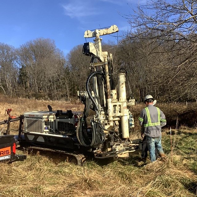 A man operates treaded equipment with hoses and a drill.