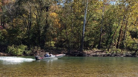 A river scene of a clear river and aluminum flat bottom boat under power going upstream.