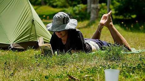 a woman reads a book on the grass outside her tent