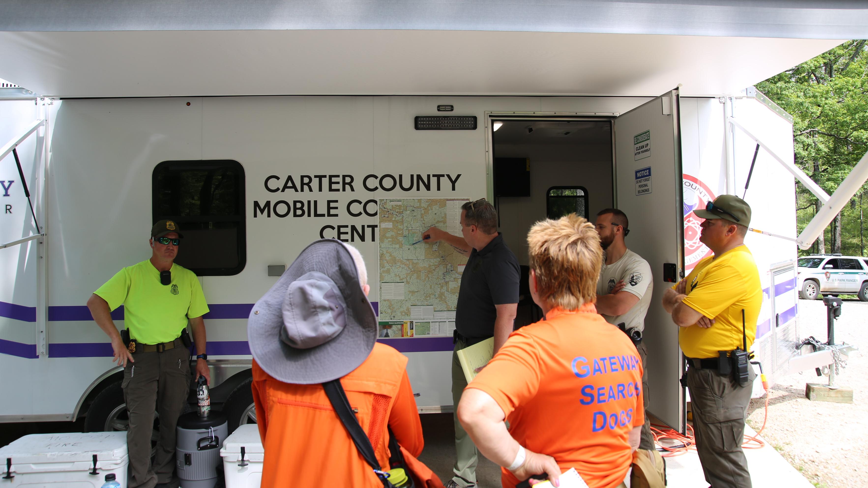 A group of people stand around a mobile command center, looking at a map.