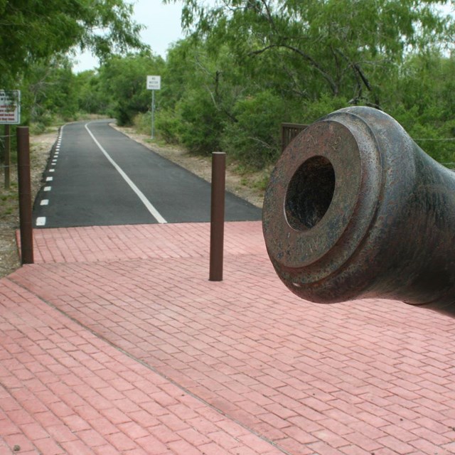 View of hike and bike trail into park with a replica cannon in the foreground.