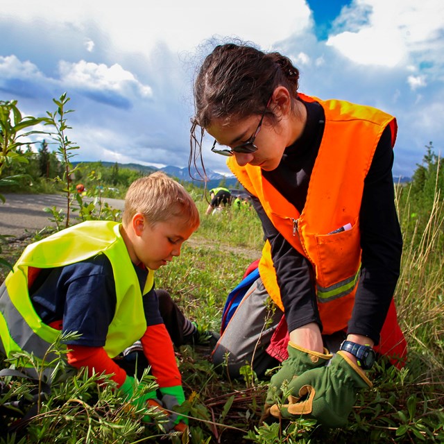 a young boy and girl in safety vests pull weeds