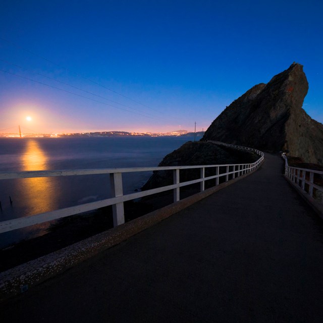 A full moon merges with the glow of Bay Area cities viewed from Point Bonita