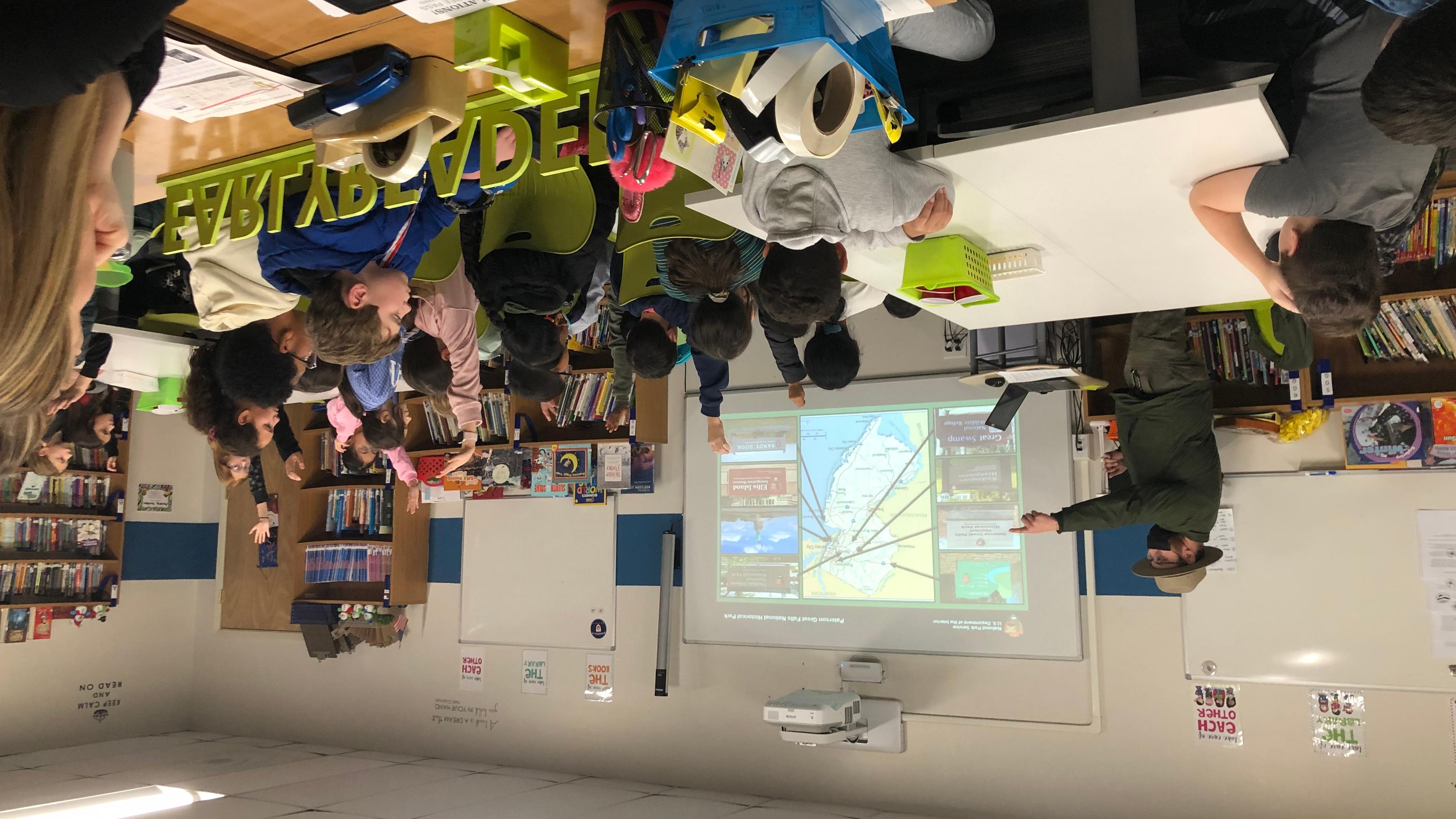 Park Ranger in a classroom pointing towards students with raised hands