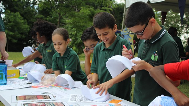 Children in green school shirts color flyers and baseball caps