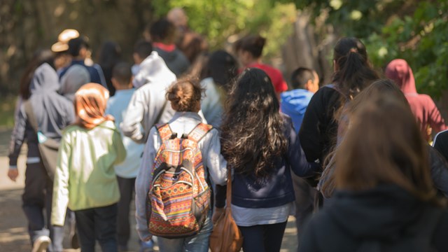 A group of students walking through the woods with a Park Ranger, facing away from the camera