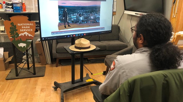A park ranger watches a television displaying a video titled "Paterson's Power Lines"