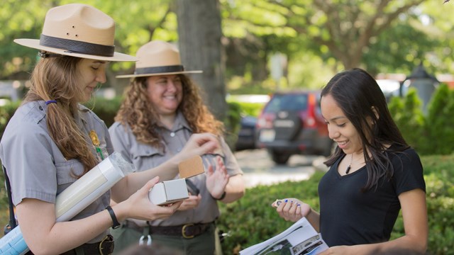 Park rangers handing written resources to a smiling woman
