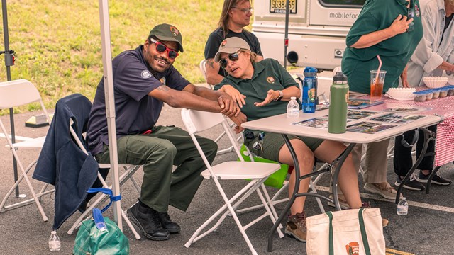 Two people in National Park Service marked clothing talk at a table at a community event