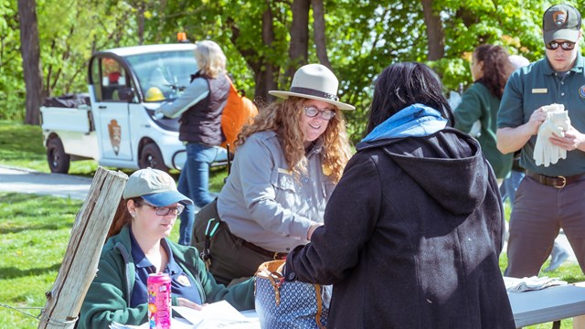 Park rangers assist a woman with information, her purse open on the outdoor table