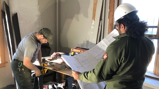 Park rangers in maintenance clothing hold tools & blueprints during office construction