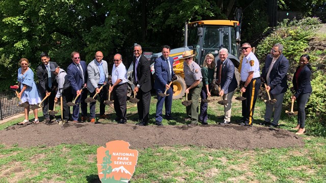 A park ranger & suited community partners shovel dirt at a groundbreaking ceremony