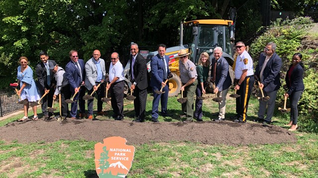 A park ranger & suited community partners shovel dirt at a groundbreaking ceremony