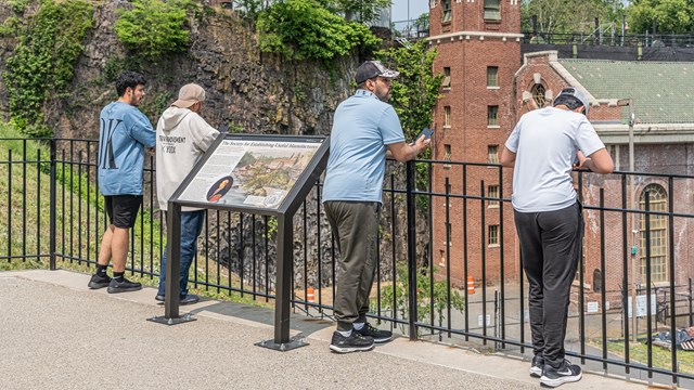 Visitors stand at an overlook railing beside a wayside information panel