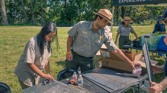 Park rangers staff an outdoor chalk art activity table & tent